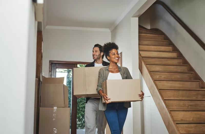 Excited happy young couple moving into new home together while carrying packing household boxes smiling positive cheerful husband wife lovely modern real estate property