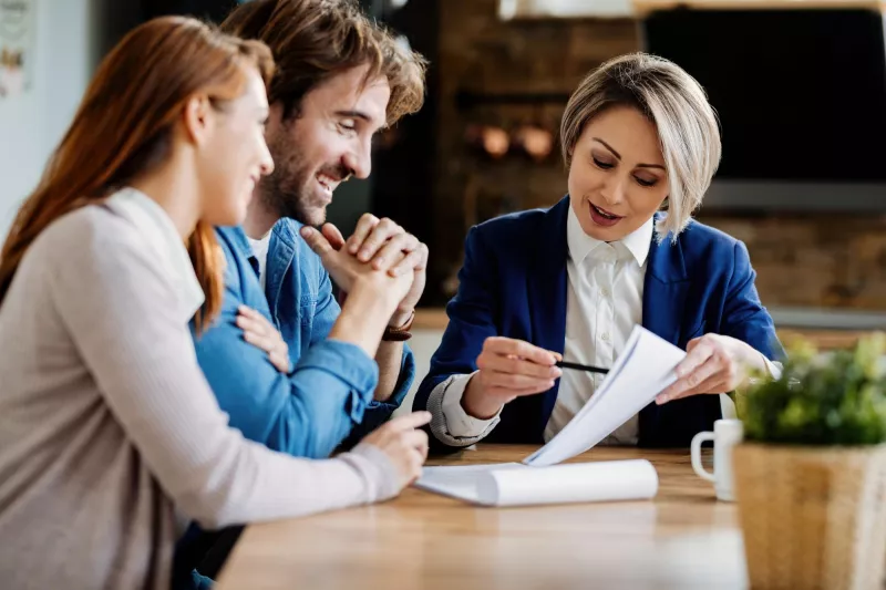 Real estate agent young couple going through lease agreement while having meeting home